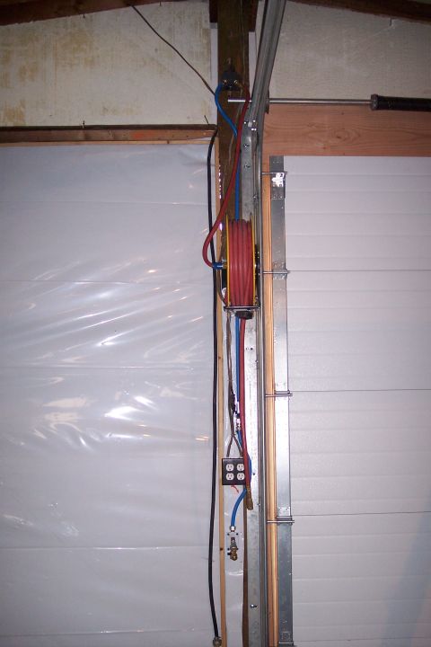 1990 Ford Bronco - A red air hose reel is mounted on a vertical track next to a garage door. Electrical outlets and blue and red air lines are also visible.