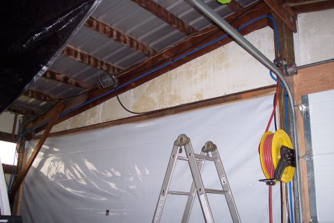 1990 Ford Bronco - This image shows the interior of a garage or workshop. A large white tarp covers a section of the wall, and a silver A-frame ladder stands…