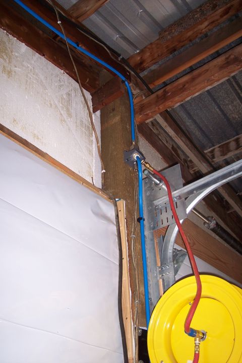 1990 Ford Bronco - A blue pneumatic pipe runs along the ceiling joists and down a wooden beam, connected to a red air hose that is wound onto a yellow reel. T…