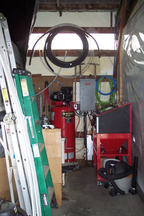 1990 Ford Bronco - An indoor scene shows various tools and equipment, including an air compressor, ladders, and a sandblaster, arranged in a workshop or garag…