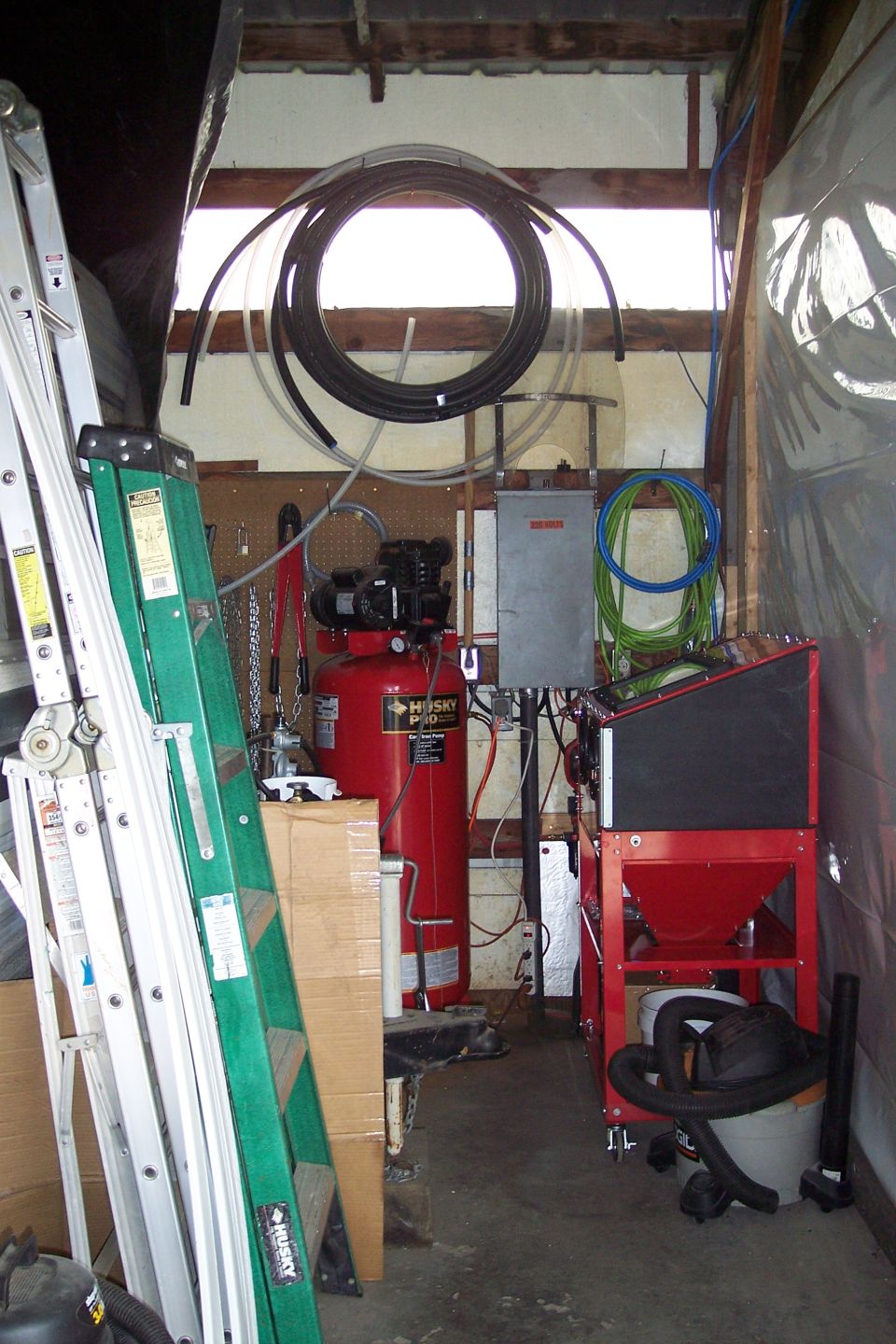 Workshop scene with air compressor, ladders, sandblaster, and coiled hoses.