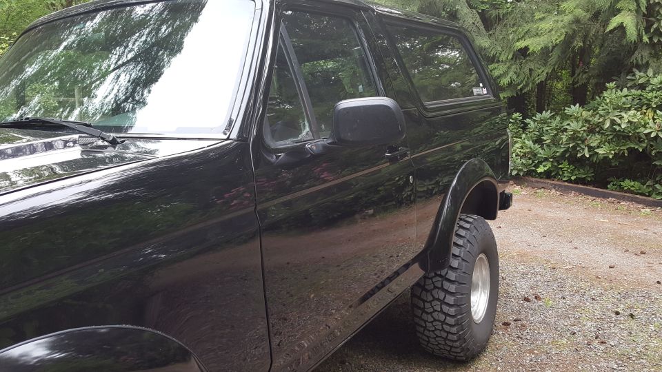Black Ford Bronco parked outdoors with trees and foliage in the background.