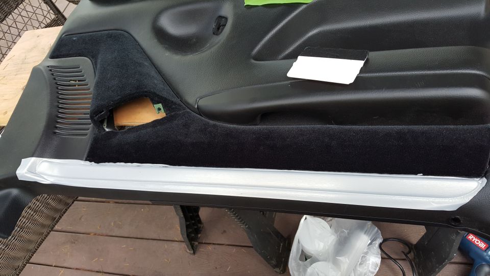 Black car door panel with carpet trim and taped silver trim piece.