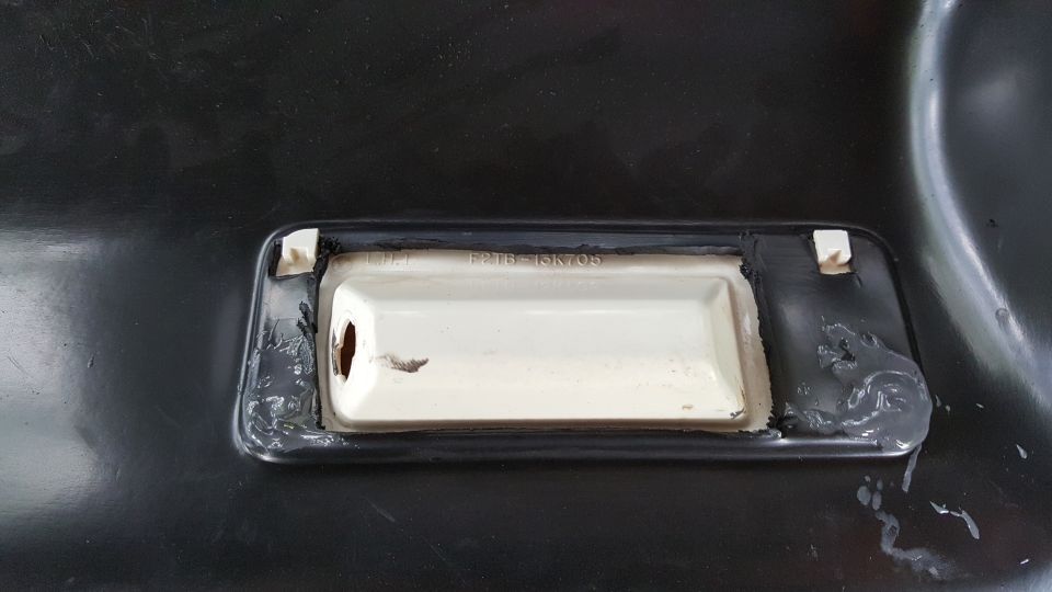 White plastic part with text F2TB-15K705 attached to black surface with sealant.