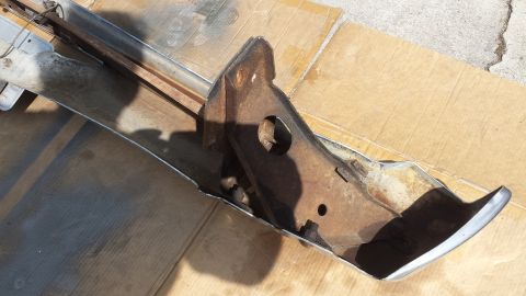 1976 Ford Ranchero - A rusty metal bumper assembly, likely from a classic vehicle, is shown resting on a cardboard surface outdoors. The chrome trim is still vi…