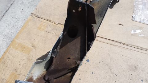 1976 Ford Ranchero - A heavily rusted metal bumper bracket is shown resting on a piece of cardboard, with concrete visible in the background. The bracket appear…