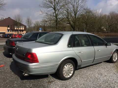 1999 Ford Fairlane - The rear passenger side of a silver four-door sedan is parked on a gravel lot next to a dark-colored sedan. The silver car has a visible ex…