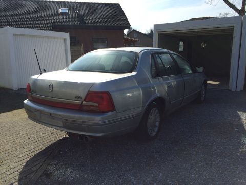 1999 Ford Fairlane - The rear passenger side of a silver sedan is parked on a gravel driveway in front of a garage. The car has dual exhaust pipes visible.