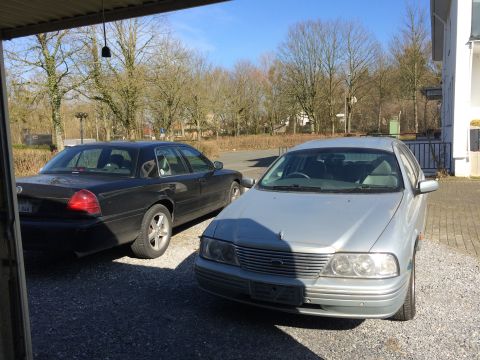 1999 Ford Fairlane - Two sedans are parked on a gravel lot under a covered structure. A black sedan is parked to the left, and a silver sedan is parked to the r…