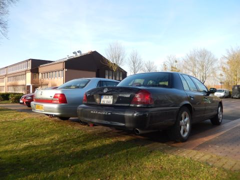 1999 Ford Fairlane - The rear passenger side of a black Ford Crown Victoria Marauder sedan is parked on a paved surface next to a grassy area. A silver sedan is…