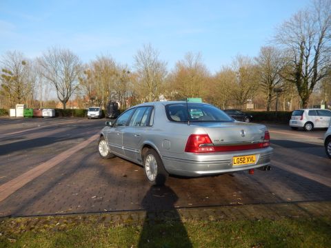 1999 Ford Fairlane - The rear passenger side of a silver 1999 Ford Fairlane sedan is parked on a brick paved lot with a grassy area in the foreground. The car h…