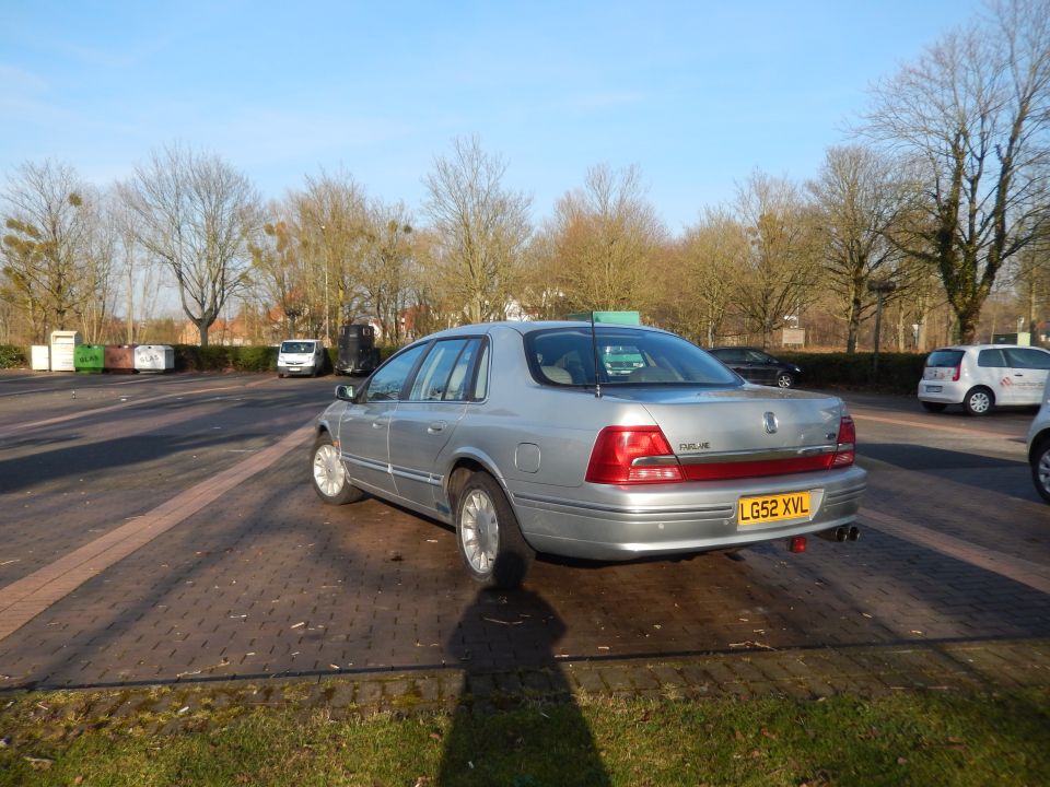 Silver 1999 Ford Fairlane sedan, rear passenger side view, parked on brick pavement.