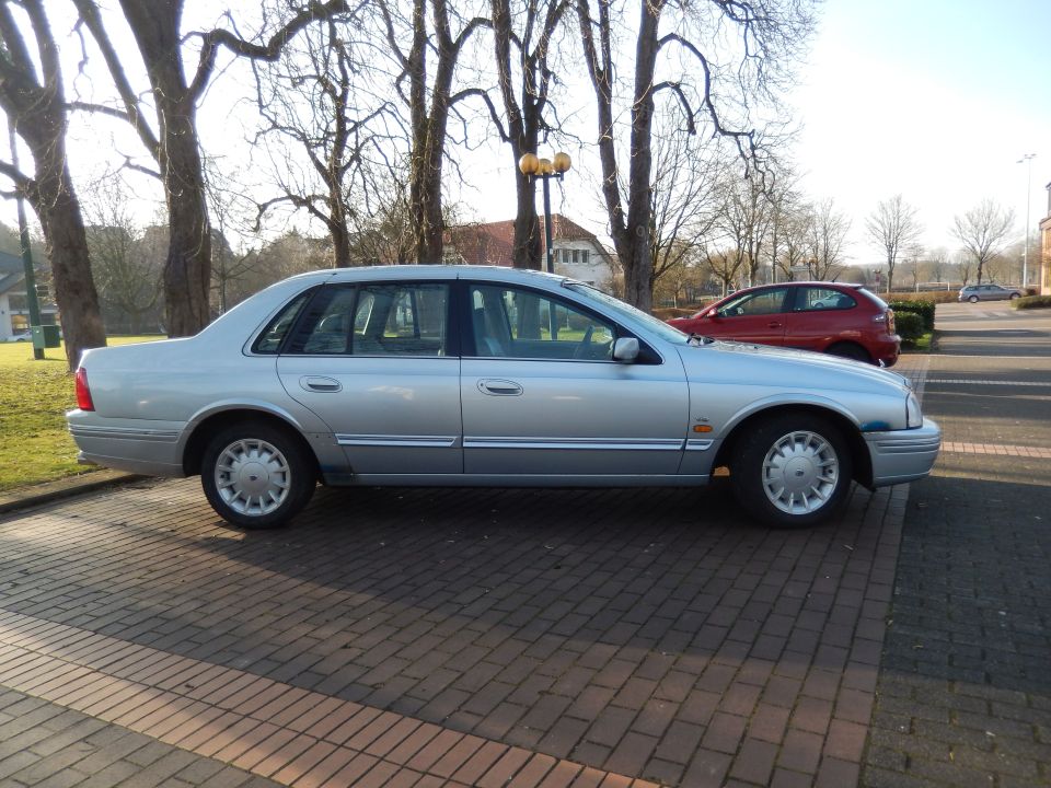 Side view of a silver 1999 Ford Fairlane sedan parked on a brick surface.