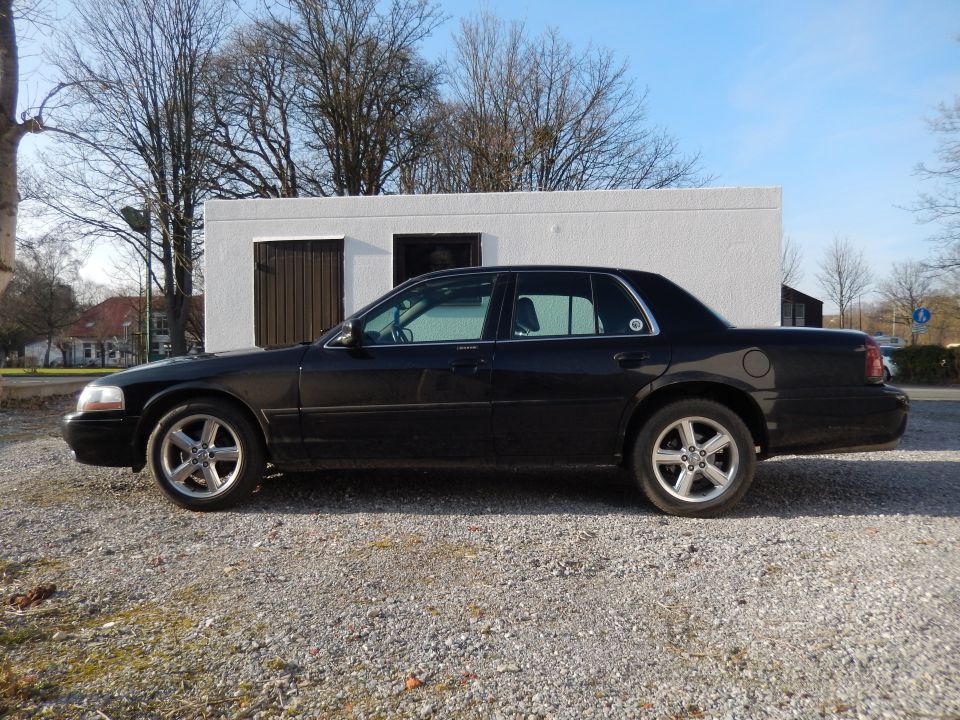 Black four-door sedan parked on gravel, side view.