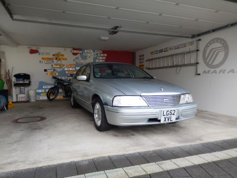 1999 Ford Fairlane - A silver 1999 Ford Fairlane sedan is parked in a garage with a map of license plates on the wall behind it. A bicycle is parked next to the…