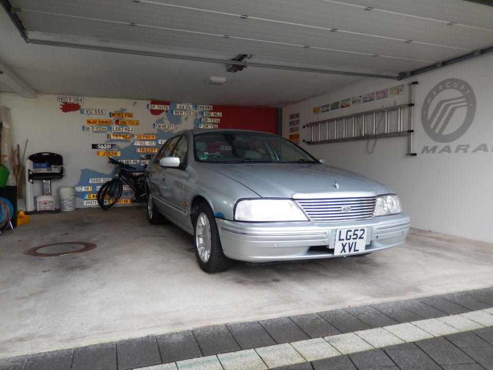 Silver 1999 Ford Fairlane sedan parked in a garage with a license plate map on the wall.