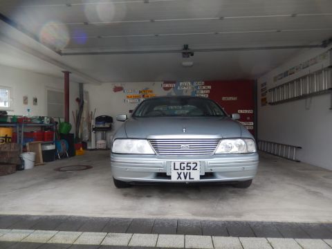 1999 Ford Fairlane - A silver 1999 Ford Fairlane is parked inside a garage. The front of the car is visible, showing its grille, headlights, and license plate.
