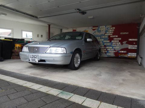 1999 Ford Fairlane - A silver 1999 Ford Fairlane is parked in a garage with a map mural on the wall behind it. The car is viewed from a 3/4 front angle, showing…