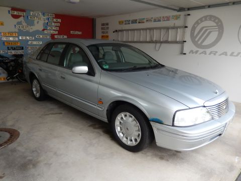 1999 Ford Fairlane - A silver sedan is parked in a garage, with a collection of license plates displayed on the wall behind it.