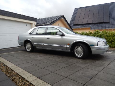 1999 Ford Fairlane - A silver sedan is parked on a paved driveway in front of a residential garage.