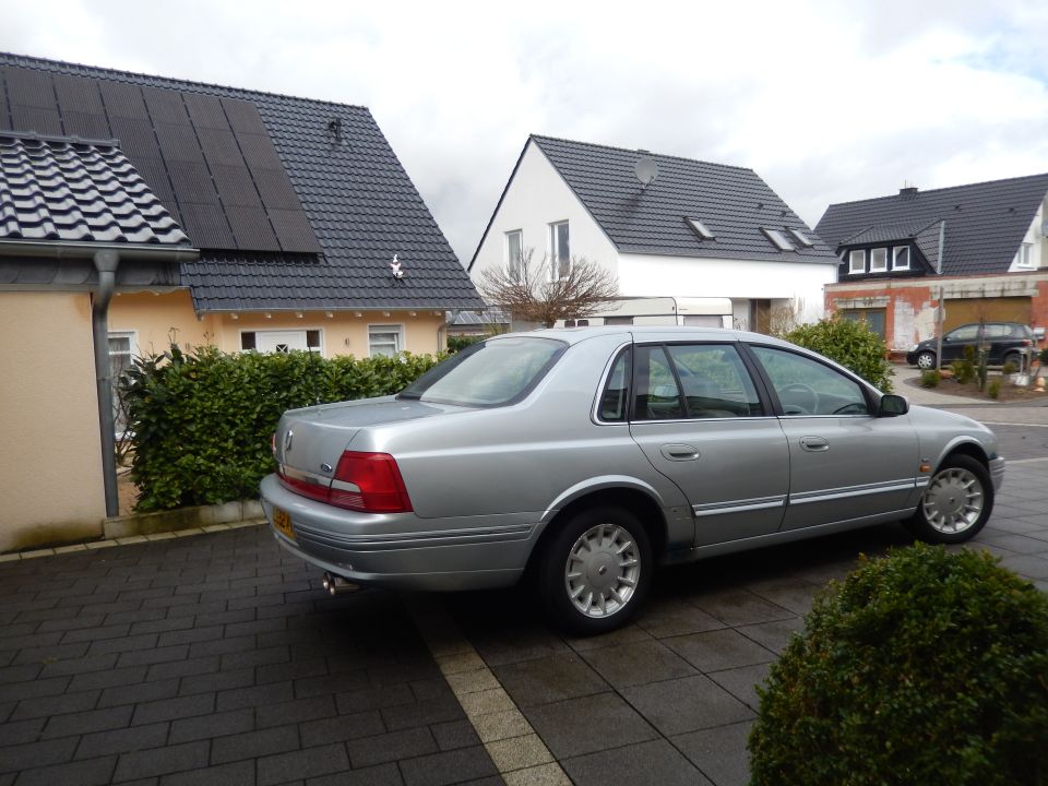 Silver sedan parked on a paved driveway, showing its side and rear