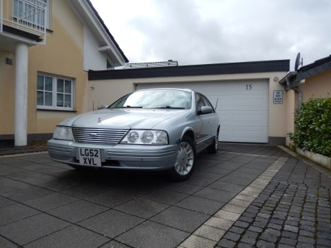 1999 Ford Fairlane - A silver sedan is parked in a driveway in front of a closed garage door.
