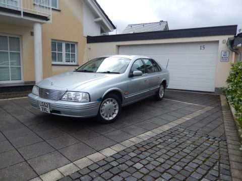 1999 Ford Fairlane - A silver 1999 Ford Fairlane sedan is parked in a driveway in front of a garage.