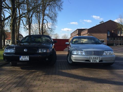 1999 Ford Fairlane - Two sedans are parked on a brick surface under a bright blue sky with scattered clouds.