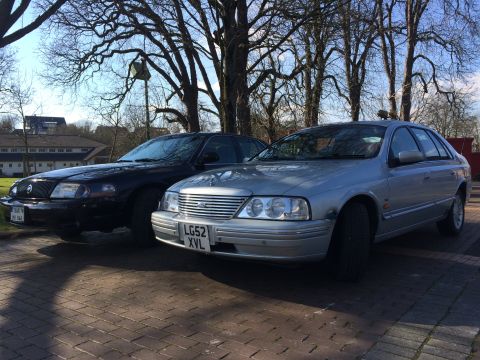 1999 Ford Fairlane - Two sedans parked outdoors on a sunny day, with trees and buildings in the background.