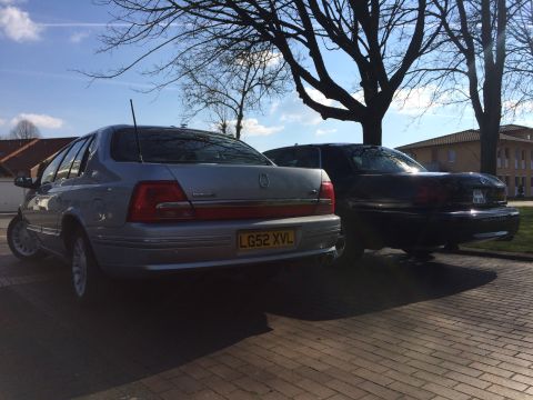 1999 Ford Fairlane - Two sedans are parked on a brick paved area under a tree on a sunny day.