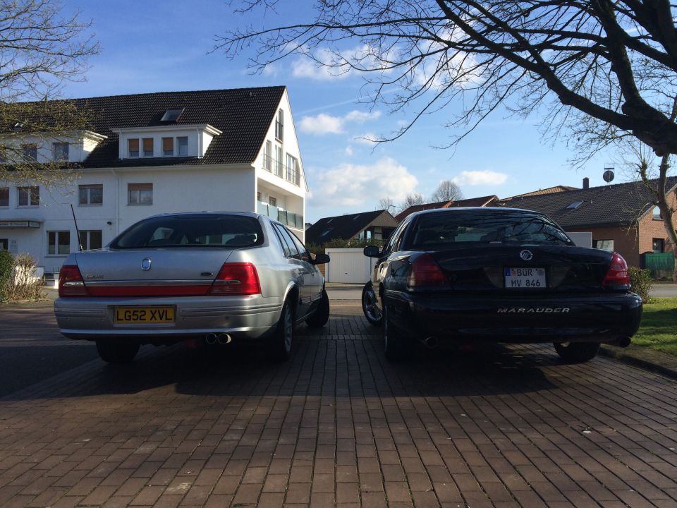 Black Mercury Marauder and silver sedan parked on brick driveway, rear view