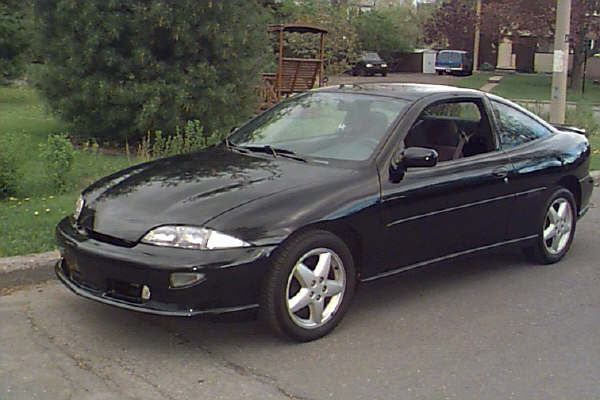 Black coupe parked on asphalt with trees and buildings in background