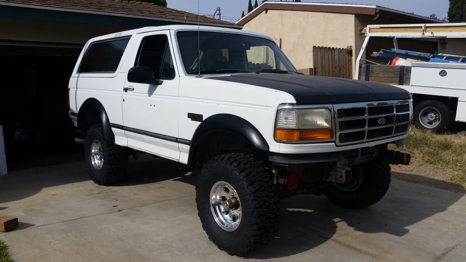 White 1992 Ford Bronco with black hood and fender flares, lifted on large tires