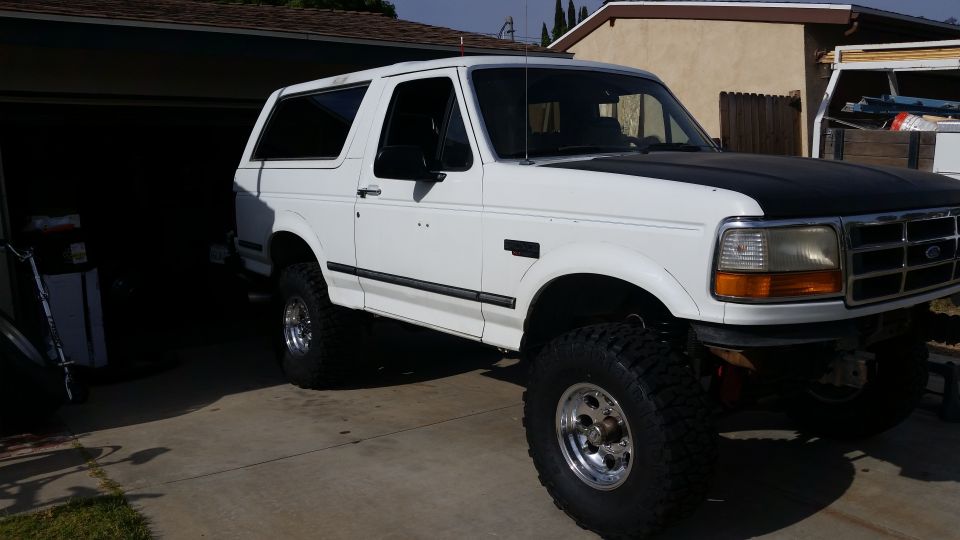 White Ford Bronco with black hood, lifted suspension, and aftermarket wheels parked in a driveway