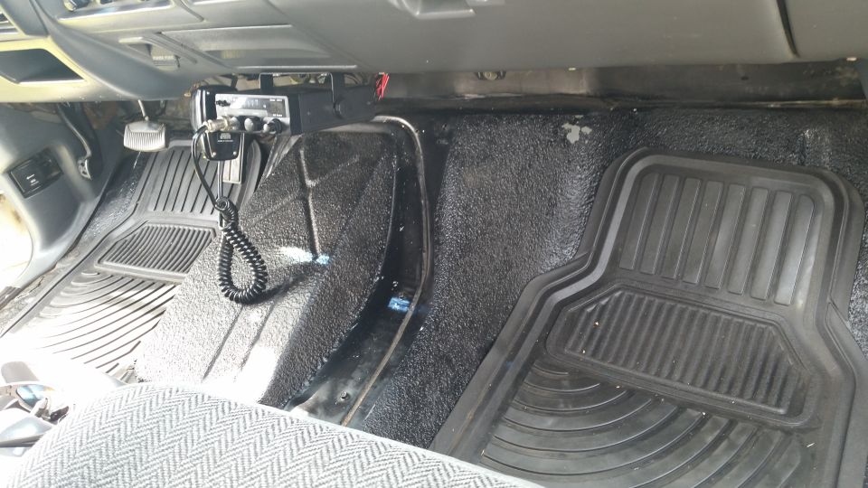 Interior view of a vehicle showing floor mats, pedals, and a CB radio mounted under the dashboard