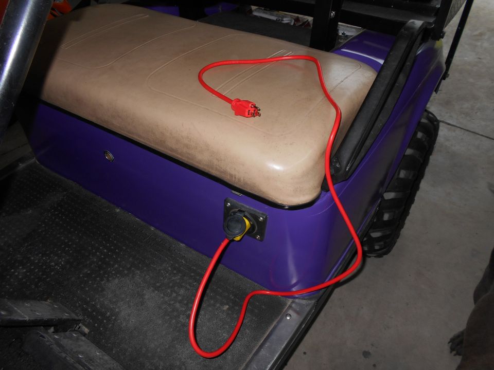 Golf cart interior with tan seats and purple body, red charging cord plugged into side