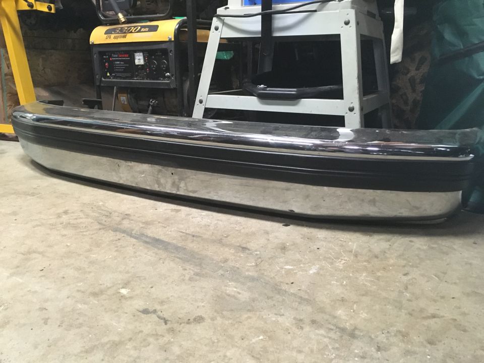 Chrome bumper with a black rubber strip, resting on a concrete floor