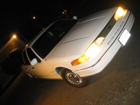 1994 Ford Crown Victoria - A white 1994 Ford Crown Victoria is shown at a 3q front angle with its headlights illuminated.