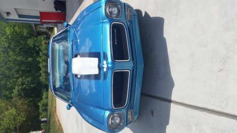 1970 Pontiac Trans Am - A blue Pontiac Firebird is parked on a concrete driveway in front of a building and trees.