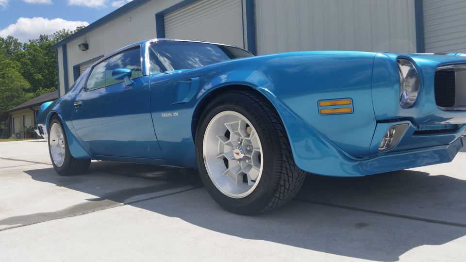 Blue 1970 Pontiac Trans Am coupe with white wheels parked in front of a garage