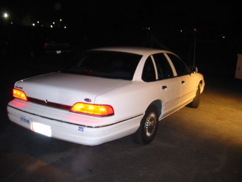1994 Ford Crown Victoria - The rear of a white sedan is illuminated by headlights at night.