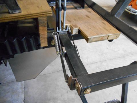 1992 Ford Bronco - Close-up of a vehicle lift mechanism, showing a wooden platform, spring, and metal components. The Supermotors logo is visible.