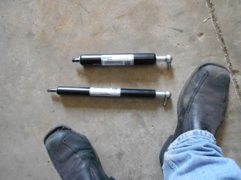1992 Ford Bronco - Two black gas struts are laid out on a concrete surface, with a person's feet visible in the foreground.