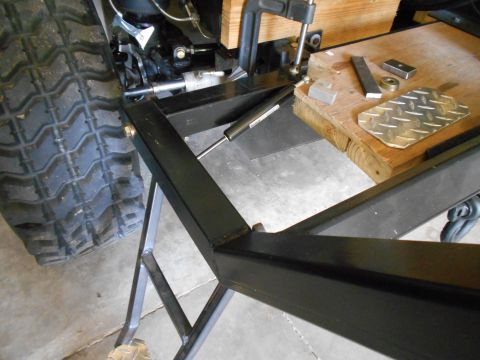 1992 Ford Bronco - Close-up of a tire and metal frame assembly, a gas strut and clamp, with various metal parts on a wooden surface.