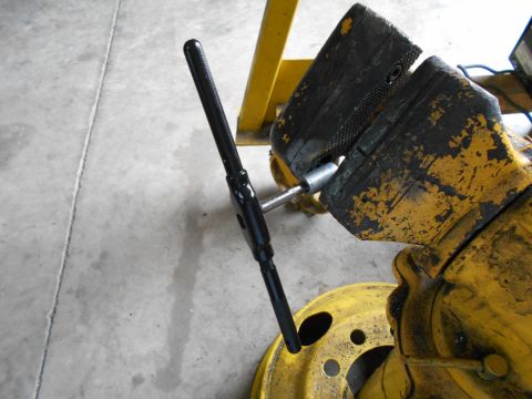 1992 Ford Bronco - A tap wrench is secured in a vise, with a yellow wheel rim visible in the foreground.