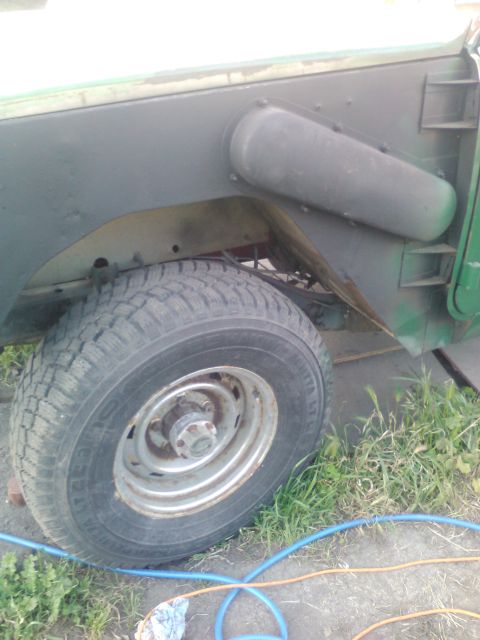 1991 Ford Bronco - A close-up view of the rear passenger side wheel well of a green vehicle, showing the tire, wheel, and part of the fender. A dark gray oval…