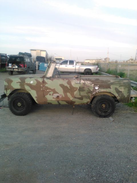 1991 Ford Bronco - A weathered, camouflage-painted Jeep CJ-5 is parked on a gravel lot. The vehicle is open-top and appears to be undergoing restoration or mo…