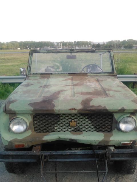 1991 Ford Bronco - The front view of a weathered, camouflage-painted off-road vehicle, possibly an International Harvester Scout, is shown parked outdoors in…