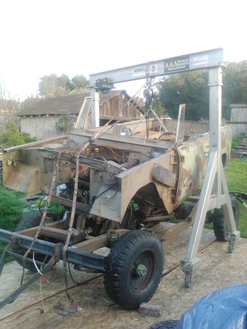 1991 Ford Bronco - A partially disassembled vehicle, possibly a 1991 Ford Bronco, is suspended by a shop crane. The vehicle's frame, engine components, and bo…
