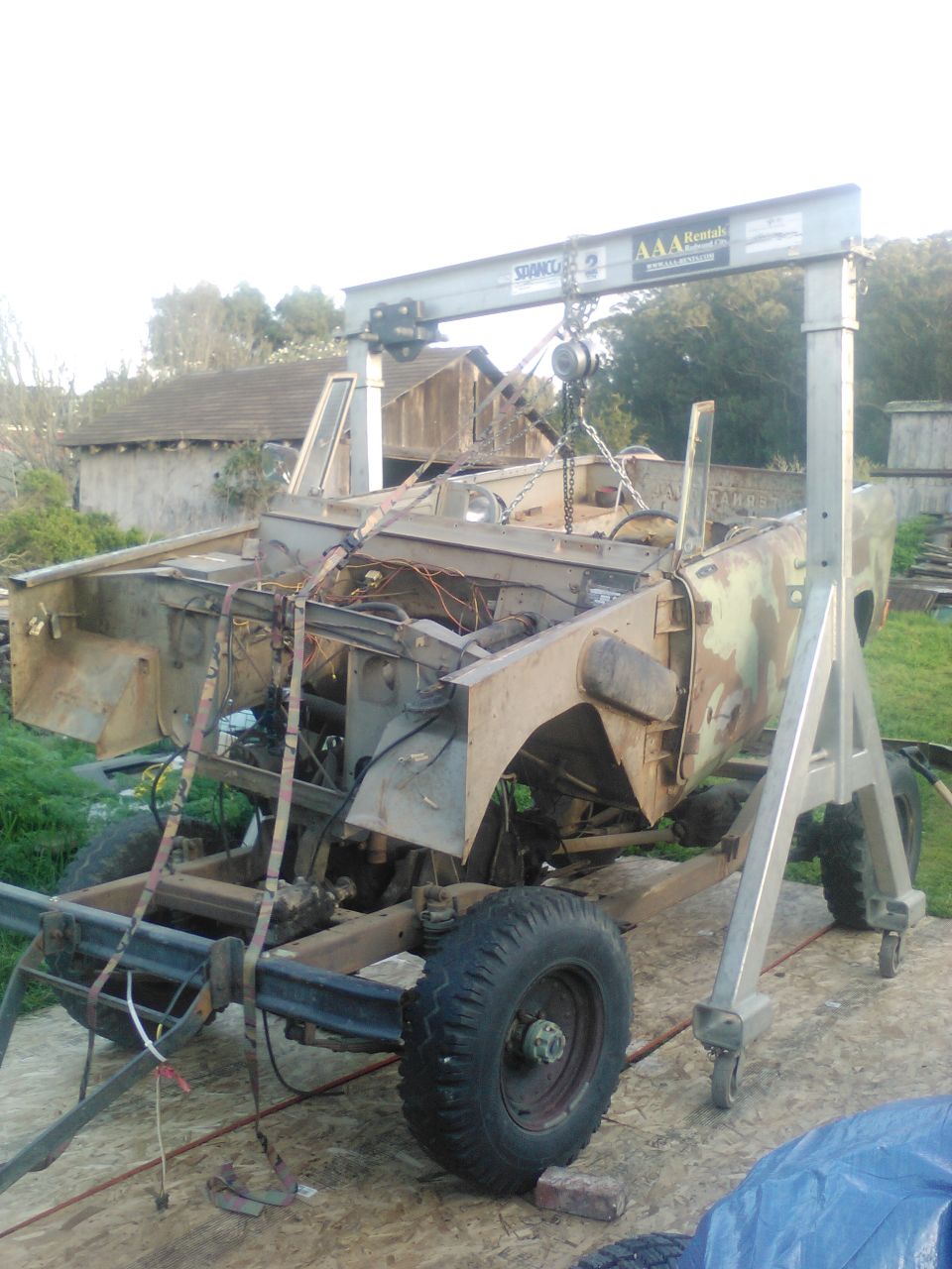 Partially disassembled vehicle suspended by a shop crane.